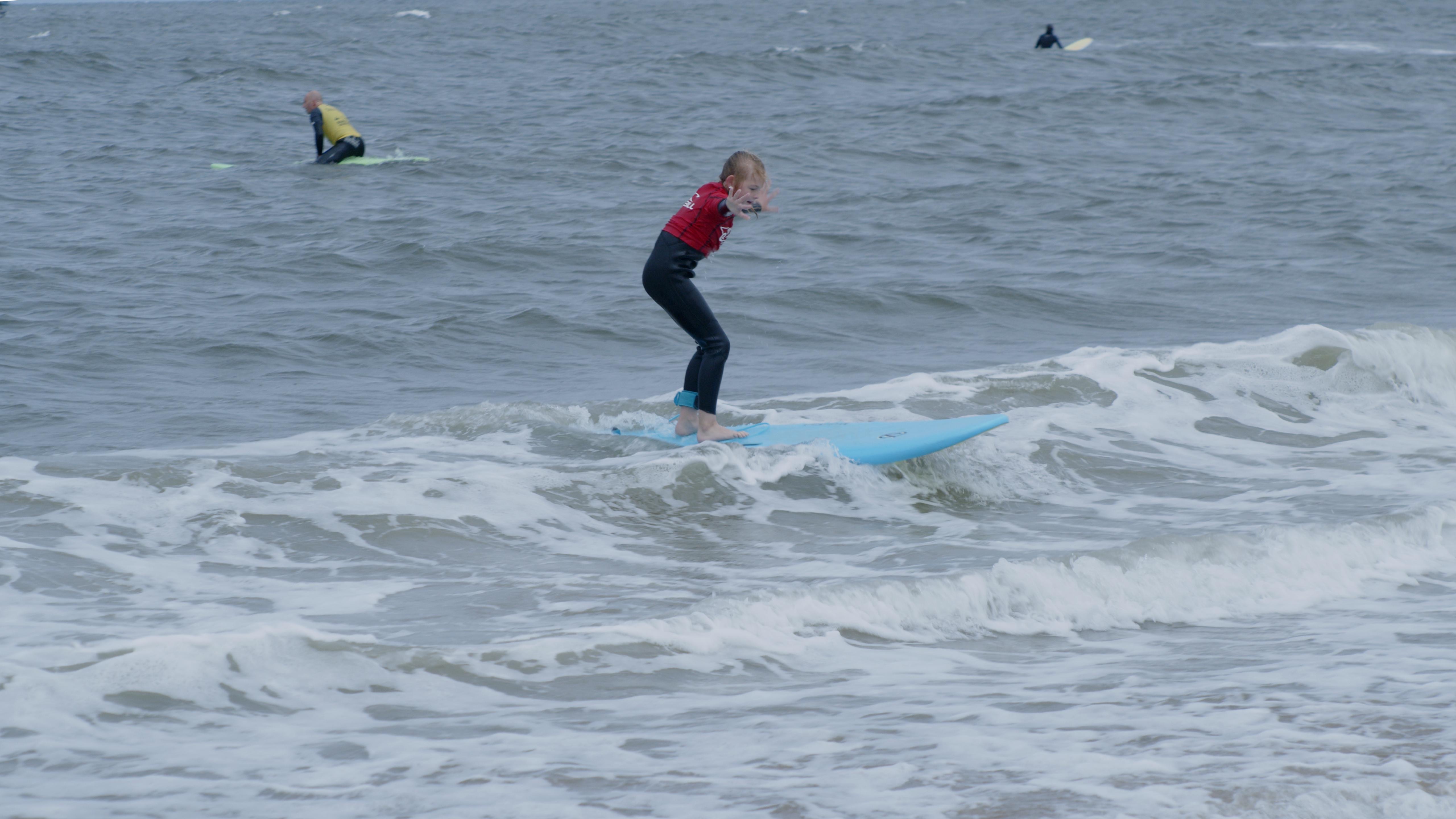 Surfinstructeur begeleidt een kind op het surfboard in zee.